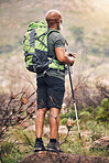 Black man, hiking and mountain with backpack for travel, adventure or trekking in the nature. African American male hiker with stick standing on rock for traveling or backpacking in the outdoors