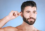 Ear, cleaning and man with cotton bud in studio for hygiene, grooming and beauty routine on blue background. Earwax, product and guy model in cosmetic, luxury and wax, removal or stick while isolated