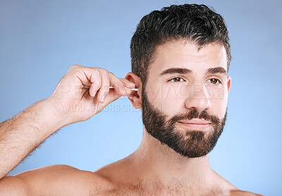 Buy stock photo Ear, cleaning and man with cotton bud in studio for hygiene, grooming and beauty routine on blue background. Earwax, product and guy model in cosmetic, luxury and wax, removal or stick while isolated