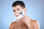 Shaving, grooming and portrait of a man with cream for beard isolated on a blue background. Skincare, beauty and model with razor to shave hair on face with foam for a clean facial look on a backdrop