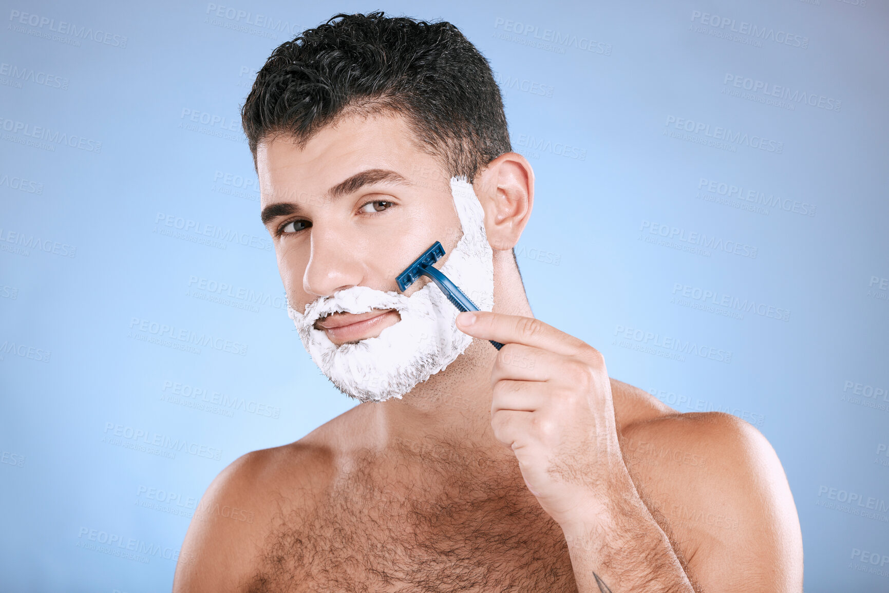 Buy stock photo Shaving, grooming and portrait of a man with cream for beard isolated on a blue background. Skincare, beauty and model with razor to shave hair on face with foam for a clean facial look on a backdrop