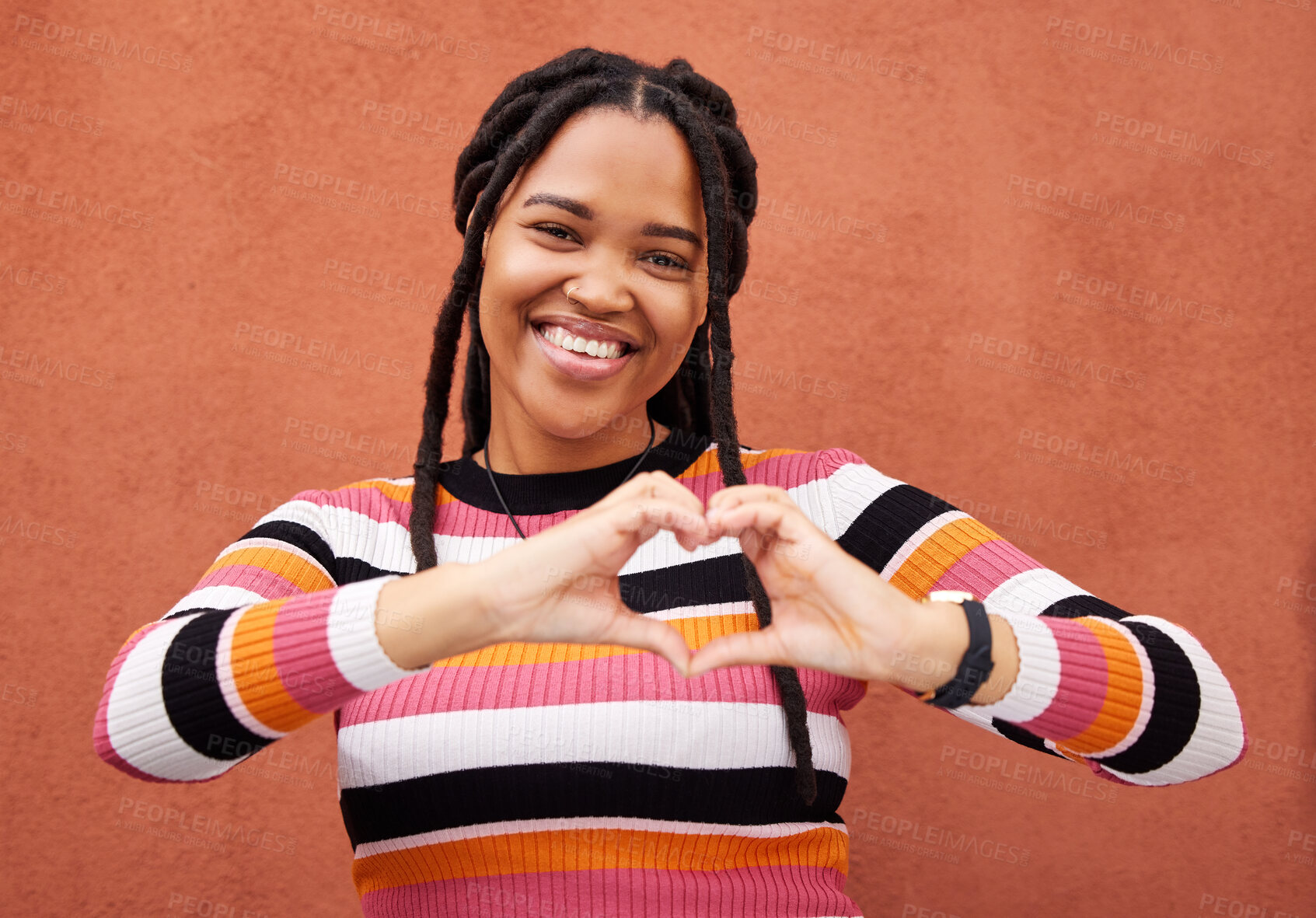 Buy stock photo Happy, heart and portrait black woman by a wall in the city while on a walk on a weekend trip. Happiness, smile and African female with a love emoji or hand gesture in town on holiday or vacation.