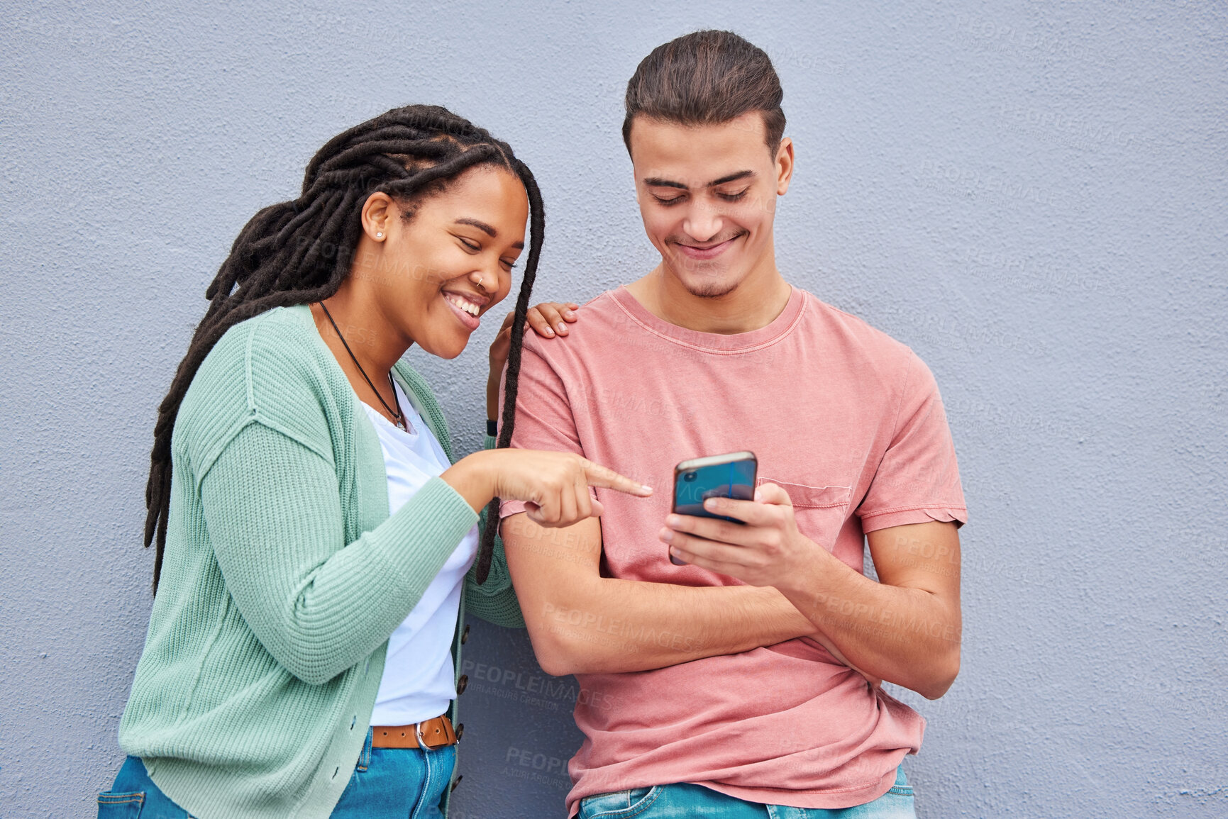 Buy stock photo Man, woman and phone by wall for meme, social media or blog post with happiness together in city. Interracial couple, smartphone and happy with smile, comic and funny video on internet app in metro