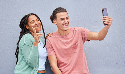 Buy stock photo Young happy couple, selfie and smile by wall with phone, profile picture and happiness in city. Influencer, man and black woman with smartphone, social media and peace sign by background in metro