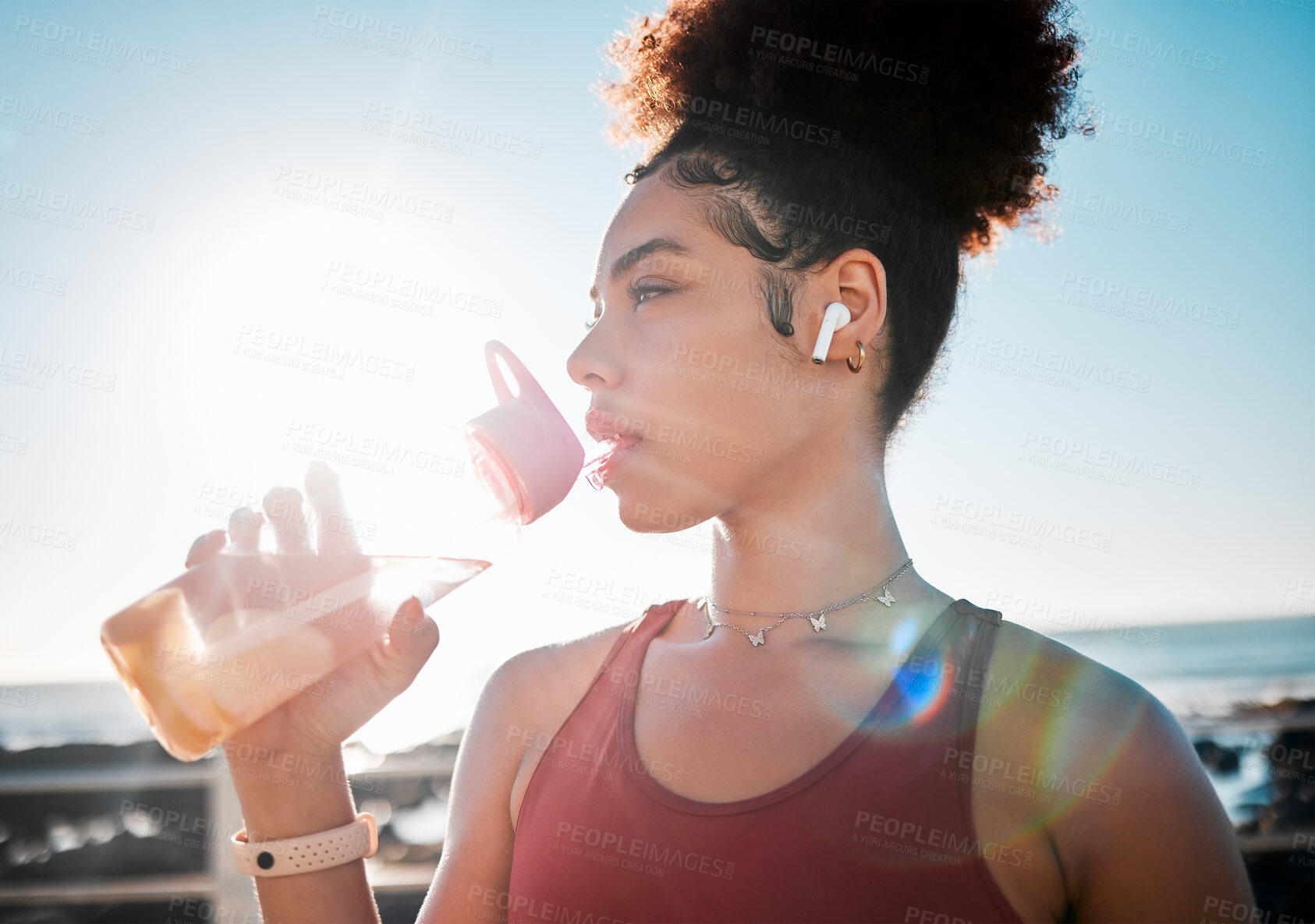 Buy stock photo Drinking water, fitness and black woman on beach exercise, listening to music and cardio training in blue sky lens flare.  Liquid bottle for diet, goals and tired sports runner or USA person by ocean