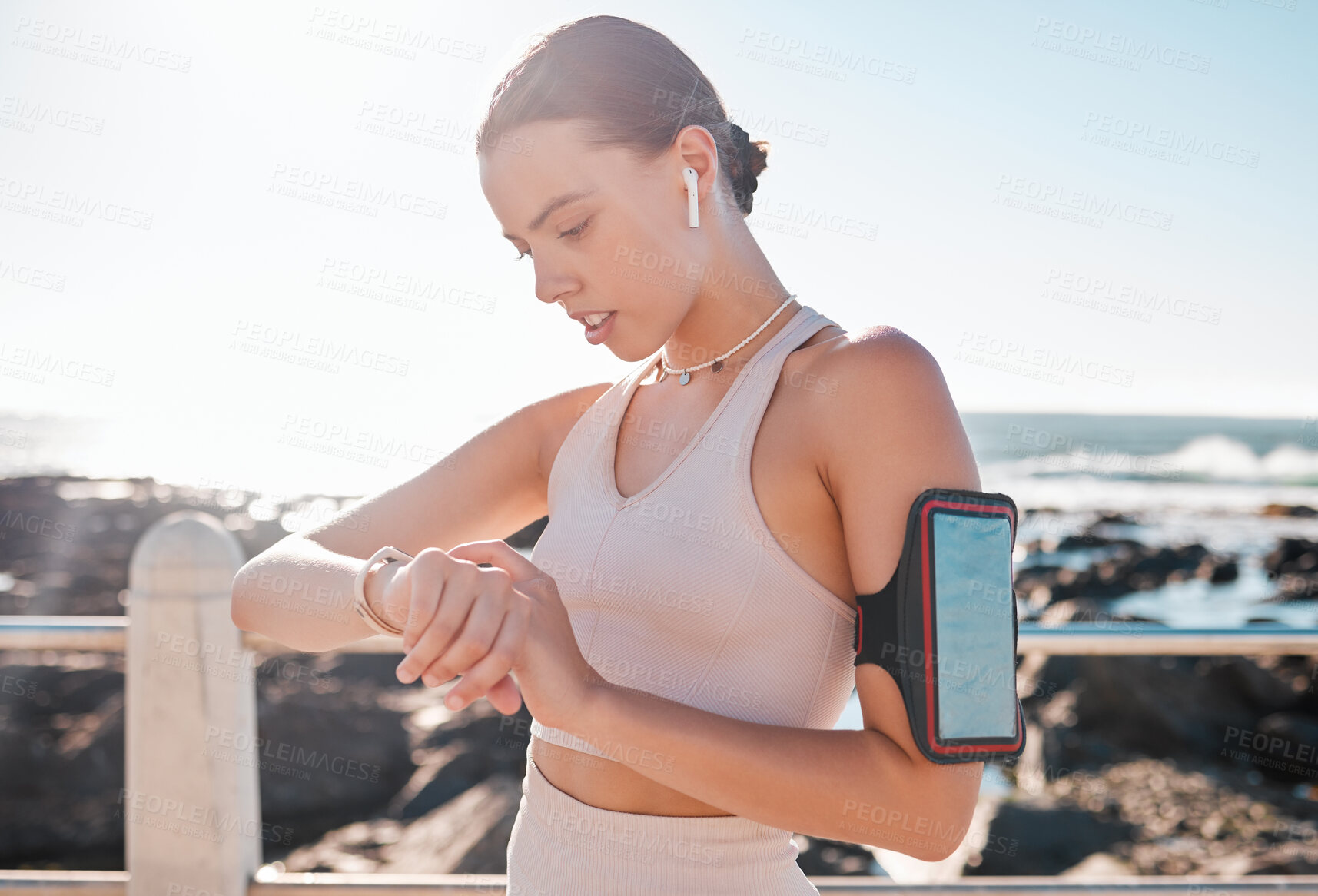 Buy stock photo Fitness time, smartwatch and woman with headphones checking running goals by the sea. Ocean, exercise app and workout timer with a runner by ocean water in summer after run and sports by a beach