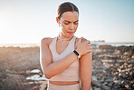 Beach, fitness and yoga, woman with shoulder pain standing on rocks at ocean. Nature, sports and injury during workout for health and wellness, muscle trauma during stretching exercise in morning.