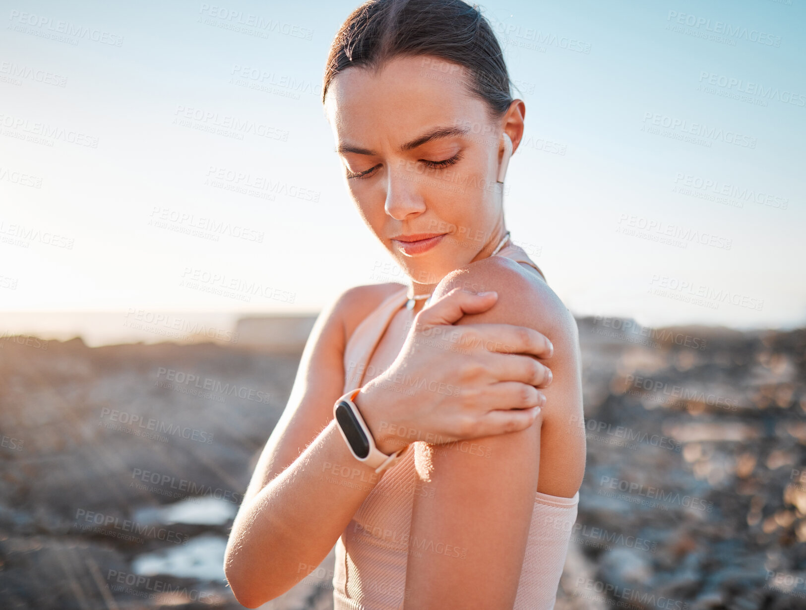 Buy stock photo Beach, fitness and woman holding shoulder pain, standing on rocks at ocean. Nature, sports and arm injury during workout for health and wellness, muscle trauma during stretching exercise in morning.