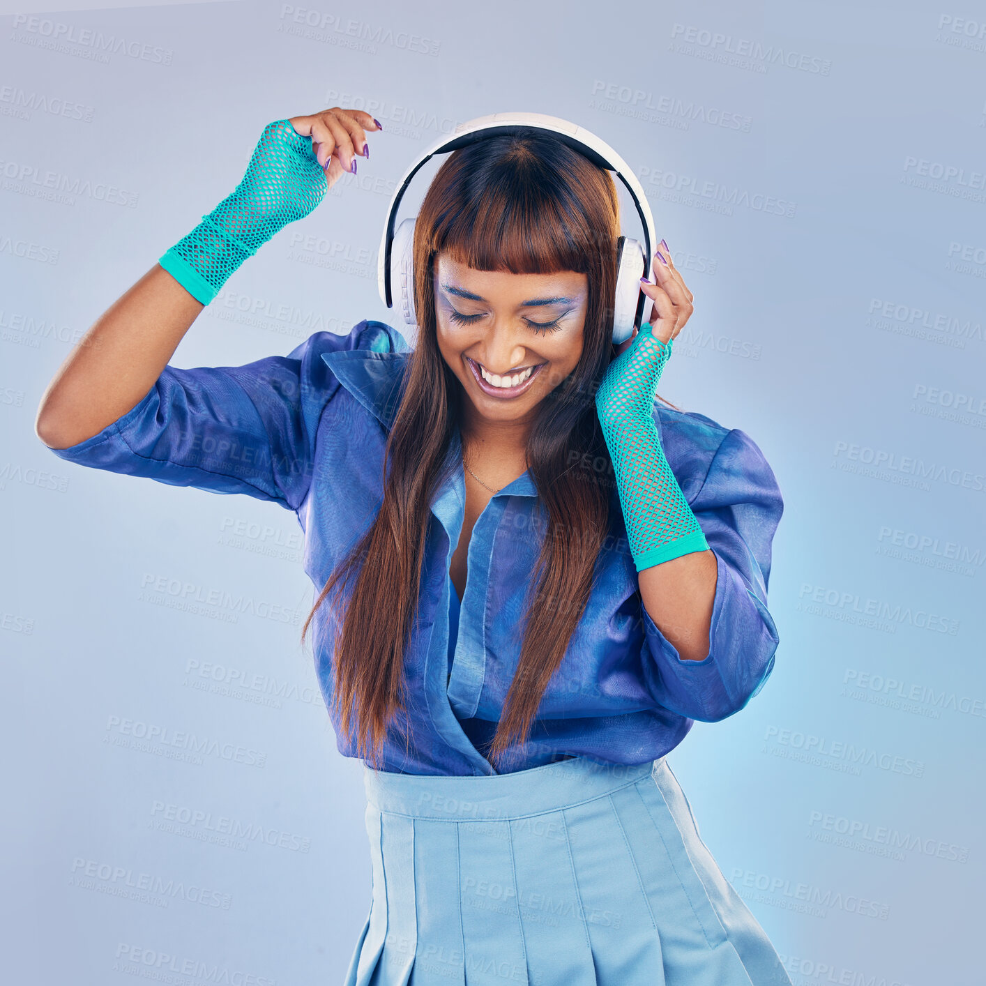 Buy stock photo Music headphones, dancing and woman with cyberpunk fashion and a smile on blue background in studio. Gen z model person with color clothes for dance while streaming and listening to futuristic audio