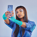 Fashion, selfie and woman with smartphone and cyberpunk neon clothing isolated on blue background. Social media, future and trendy gen z influencer from India with phone in studio for profile picture