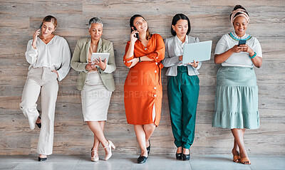 Buy stock photo Wall, business and women with devices, online reading and connection for social media, typing and communication. Diversity, female employees and happy coworkers chatting, texting and search internet