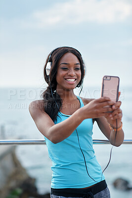 Buy stock photo Black woman, phone and headphones at beach, selfie and smile for video call, music or funny meme to relax. Runner, rest and smartphone with social network post, app and happiness on outdoor adventure