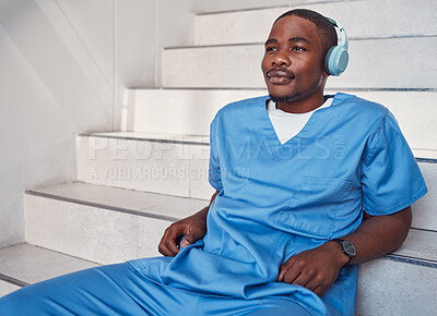 Buy stock photo Break, music and African doctor with headphones for a podcast, radio and audio on hospital stairs. Freedom, thinking and a male nurse listening to a track or songs while working in healthcare