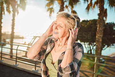 Buy stock photo Happy, music and singing with old woman at beach for streaming, freedom and summer break. Internet, technology and headphones with senior lady listening to online radio for podcast, audio and media