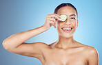 Cucumber, woman and portrait face for beauty, clean wellness diet and blue studio background. Happy model, eyes and green fruits cosmetics for detox, facial skincare and healthy aesthetic benefits 