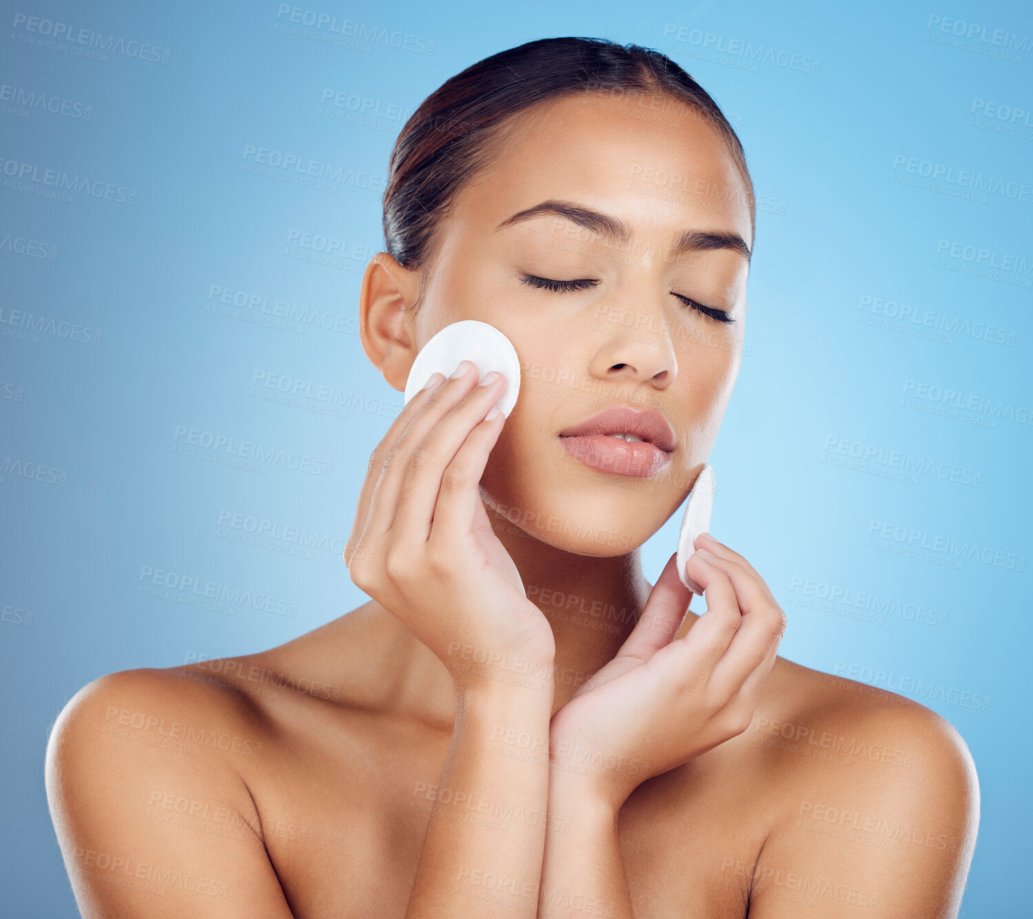 Buy stock photo Skincare, woman with cottonwool on face and eyes closed removing makeup or dirt with luxury skin product in studio. Dermatology, cosmetics and beauty spa facial for model isolated on blue background.