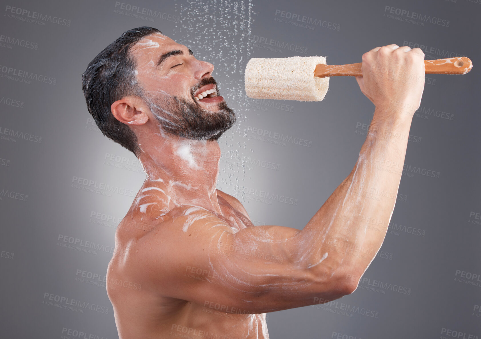 Buy stock photo Shower, cleaning and man singing with brush in studio for skincare, washing body and wellness on gray background. Beauty, bathroom and happy male do karaoke with loofah sponge, soap and water splash