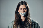 Woman, face and protest with tape on mouth for fuel prices or economy struggle against gray studio background. Portrait of female activist with covered lips in silence of speech for voice message