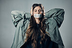 Woman, protest and tape on mouth in fear for cold war, armageddon or doomsday against gray studio background. Female activist with hands on head and message to stop or end global violence in society