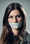 Woman, face and protest with mouth tape in Russia for cold war, armageddon or doomsday against a gray studio background. Portrait of female activist or secret Russian agent or refugee in silence