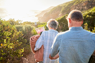 Buy stock photo Picnic, romance and senior couple walking in nature with blanket and flowers for love and valentines day. Mountain path, old man and woman holding hands on walk for romantic valentine date from back.