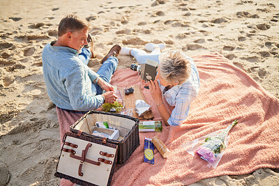 Buy stock photo Senior couple, beach and picnic basket above for romantic getaway, travel or valentines day celebration in nature. Happy elderly man and woman relax by a sandy ocean coast for date, meal or trip