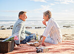 Senior couple, beach and picnic on blanket for romantic getaway, travel or valentines day celebration in nature. Happy elderly man and woman relax by a sandy ocean coast for date, basket meal or trip