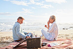 Senior couple, romantic beach picnic and smile together in summer for conversation, memory and comic time. Elderly man, old woman and basket for food, wine and outdoor for sunshine, waves and love