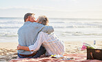Senior couple, beach picnic and kiss with hug, romance and happiness in summer for anniversary celebration. Elderly man, old woman and basket for food, wine and outdoor for sunshine, waves and love