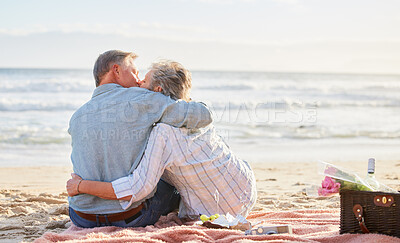 Buy stock photo Senior couple, beach picnic and kiss with hug, romance and happiness in summer for anniversary celebration. Elderly man, old woman and basket for food, wine and outdoor for sunshine, waves and love