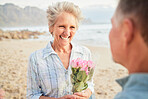 Beach, flowers and valentines day with a senior couple in celebration of love together outdoor in nature. Romance, rose or smile with a happy mature woman and man celebrating on the coast in summer