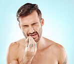 Man with tweezer, painful nose hair removal and morning routine for beauty and skincare isolated on blue background. Face, frown and grooming facial hairs, male model with tattoo on hand in studio.