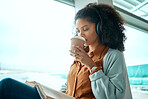 Airport, coffee and black woman reading a book by window waiting for global flight, departure and travel. International transport, lobby and girl with headphones for music, drinking beverage and read