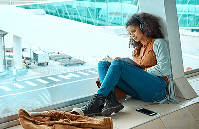 Buy stock photo Airport, travel and black woman reading a book by window waiting for global flight, departure and transport. Immigration, travelling lobby and girl relax with headphones for music, podcast and audio