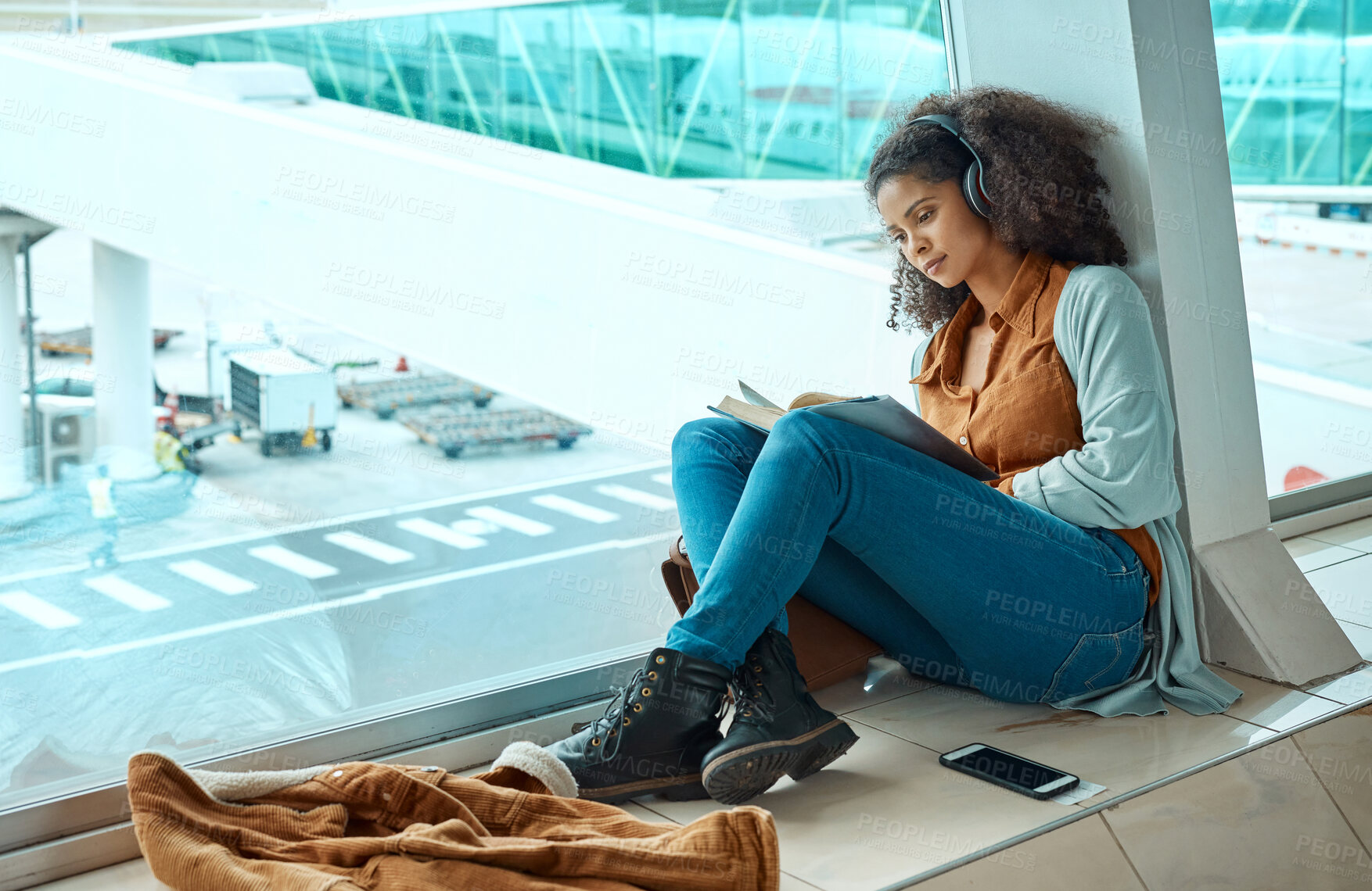 Buy stock photo Airport, travel and black woman reading a book by window waiting for global flight, departure and transport. Immigration, travelling lobby and girl relax with headphones for music, podcast and audio