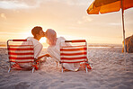 Couple, kiss and beach chairs by a ocean sunset with love, happiness and care on vacation. Sea, sunshine and kissing of happy young people together sitting by the sand feeling relax outdoor 