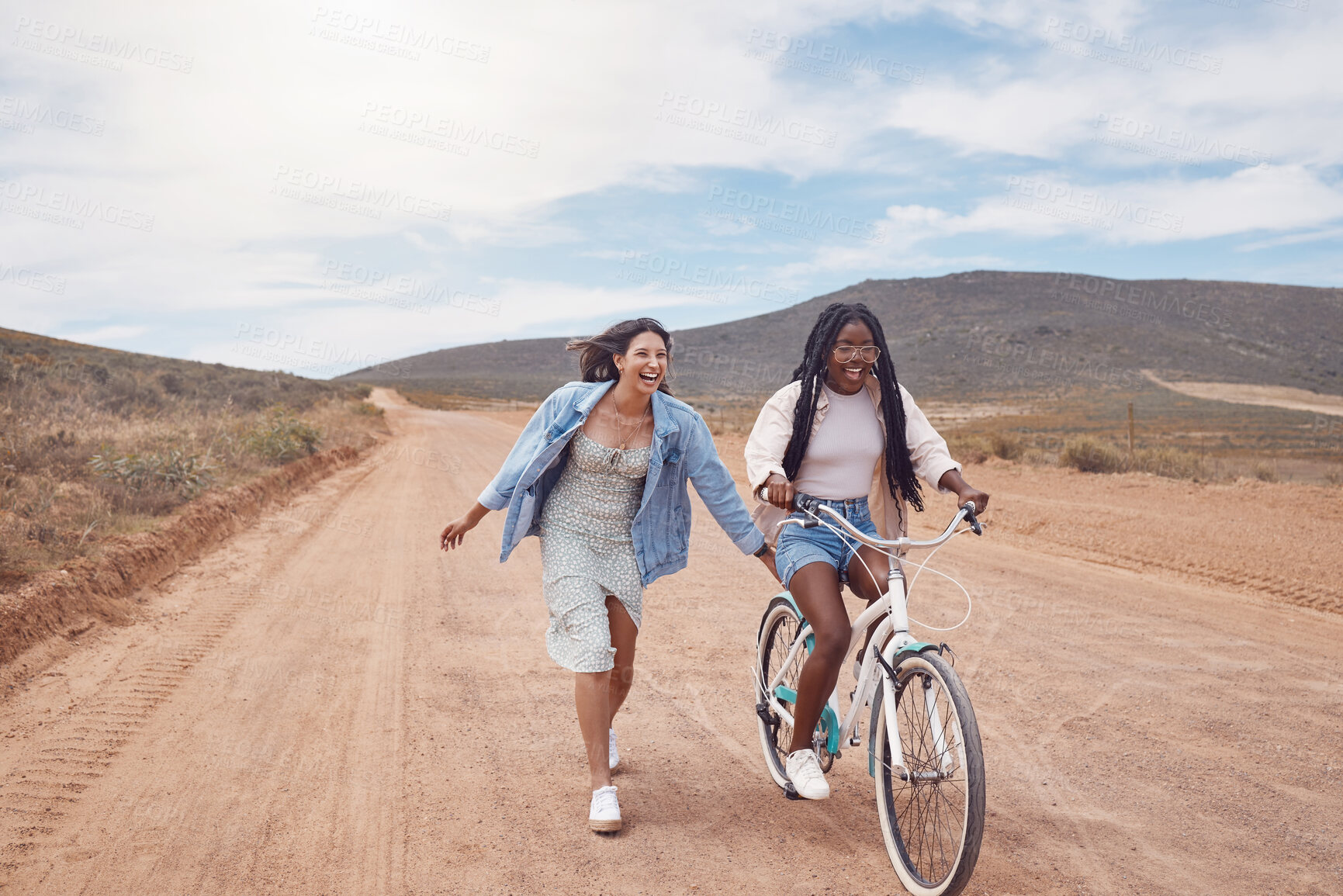 Buy stock photo Bike ride, girl friends and road trip fun of women outdoor on a desert path on summer vacation. Cycling, running and freedom of young people together with bicycle transportation feeling free 