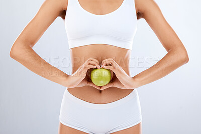 Buy stock photo Digestion, apple and woman stomach with hands in heart shape for nutrition, detox diet and studio background. Fruits, wellness and healthy abdomen body with care, love and lose weight for strong gut 