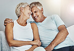 Love, laughing and retirement with a senior couple sitting in the living room of their home together. Happy, smile or relax with a mature man and woman joking while bonding on the couch in a house