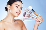 Makeup, beauty and woman with brushes in hand on blue background for cosmetics, powder and foundation. Cosmetology, salon aesthetic and face of girl with tools for application, wellness and glow