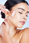 Woman, face and roller for beauty skincare, cosmetics or facial treatment against a blue studio background. Female hands with rolling tool for cosmetic anti aging routine, clean skin wellness or glow
