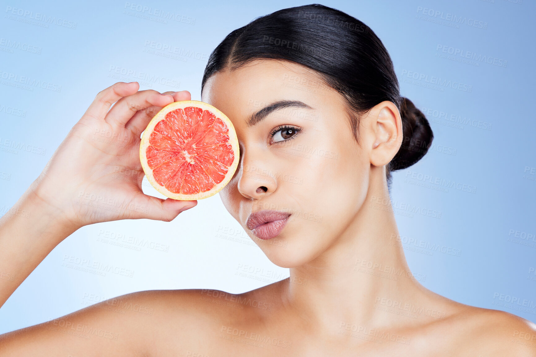 Buy stock photo Woman, face and fruit for skincare nutrition, vitamin C or healthy diet against a blue studio background. Portrait of female holding organic grapefruit for citrus health, facial or beauty wellness