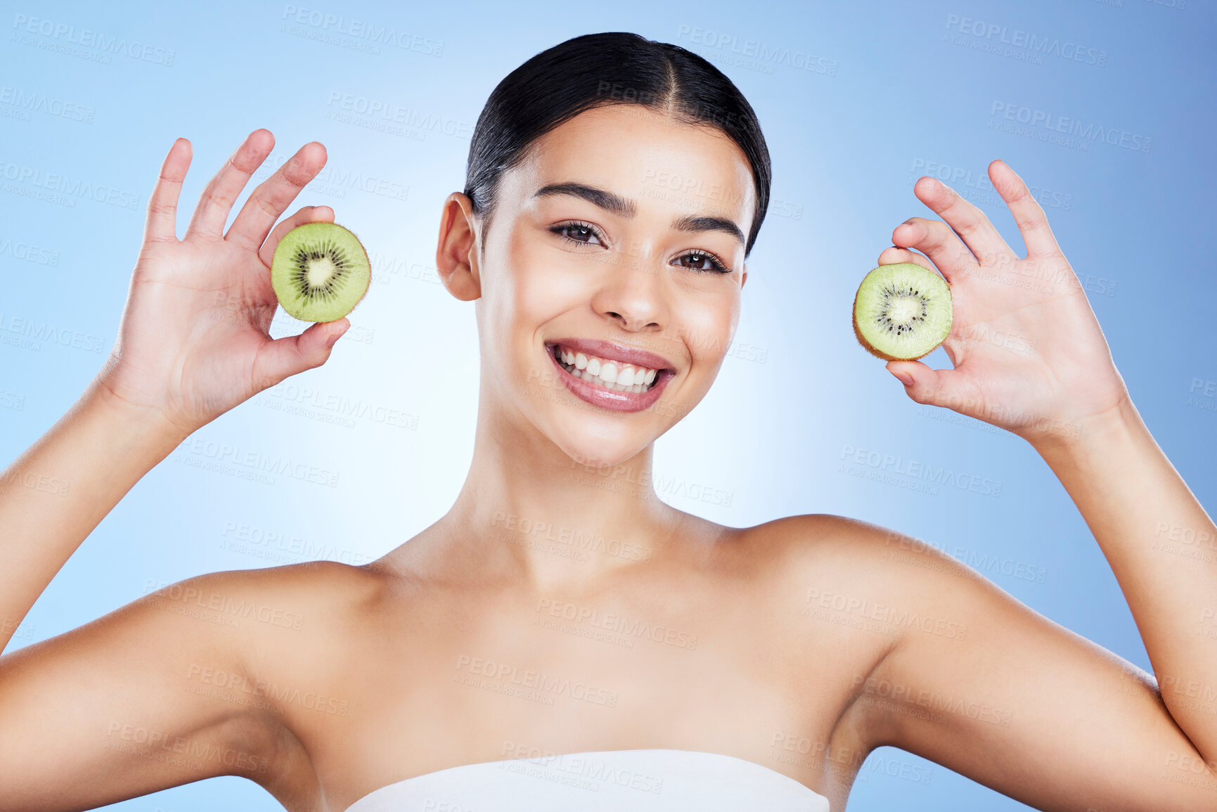 Buy stock photo Woman, face and kiwi for skincare nutrition, vitamin C or healthy diet against a blue studio background. Portrait of female with smile holding organic fruit for health, facial or beauty wellness