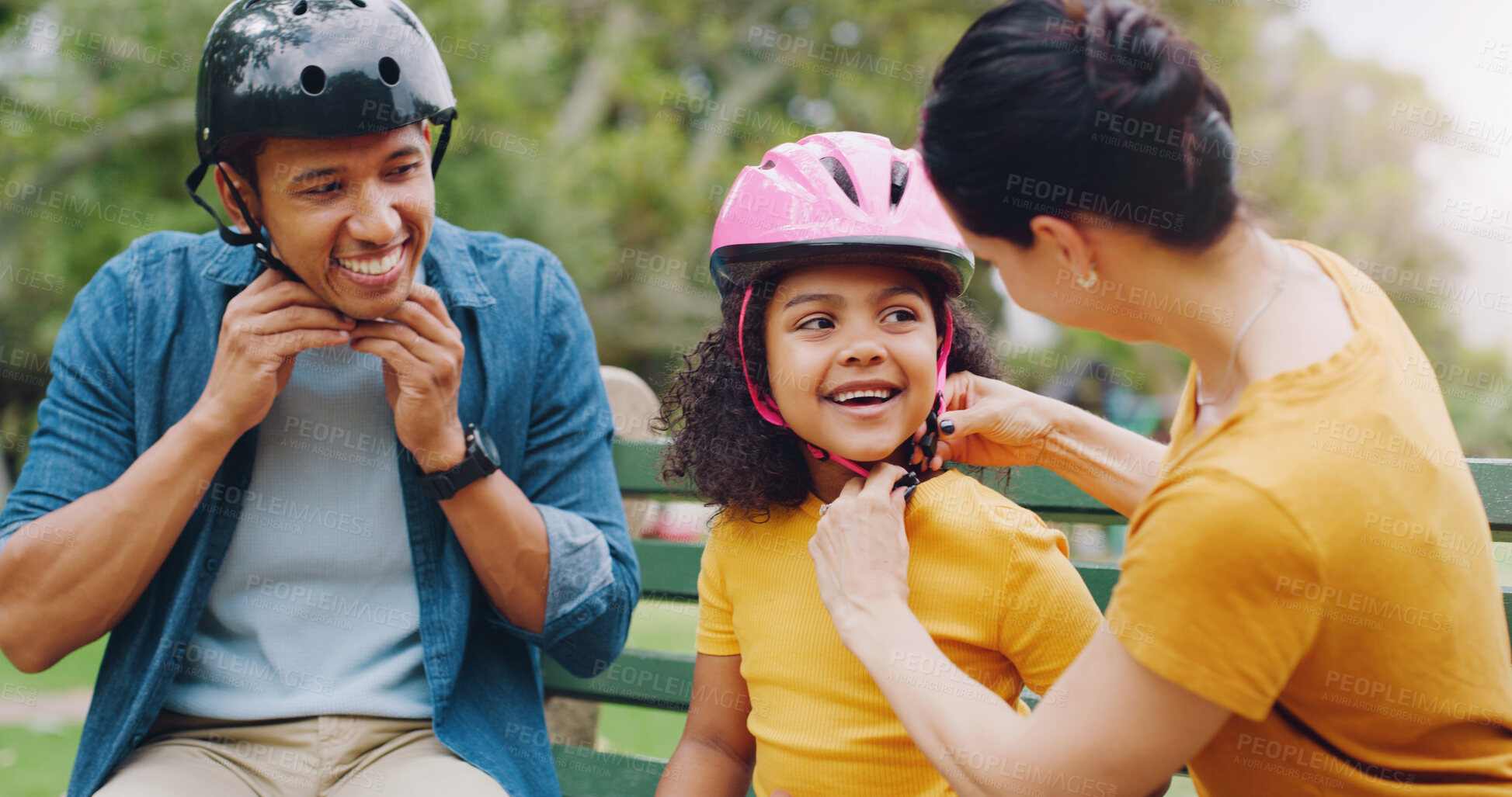 Buy stock photo Parents, park bench and helmet with child, help and safety for skating, rollerskate or bike. Interracial parents, mom and dad with helping hand, teaching and kid for bonding, learning and exercise
