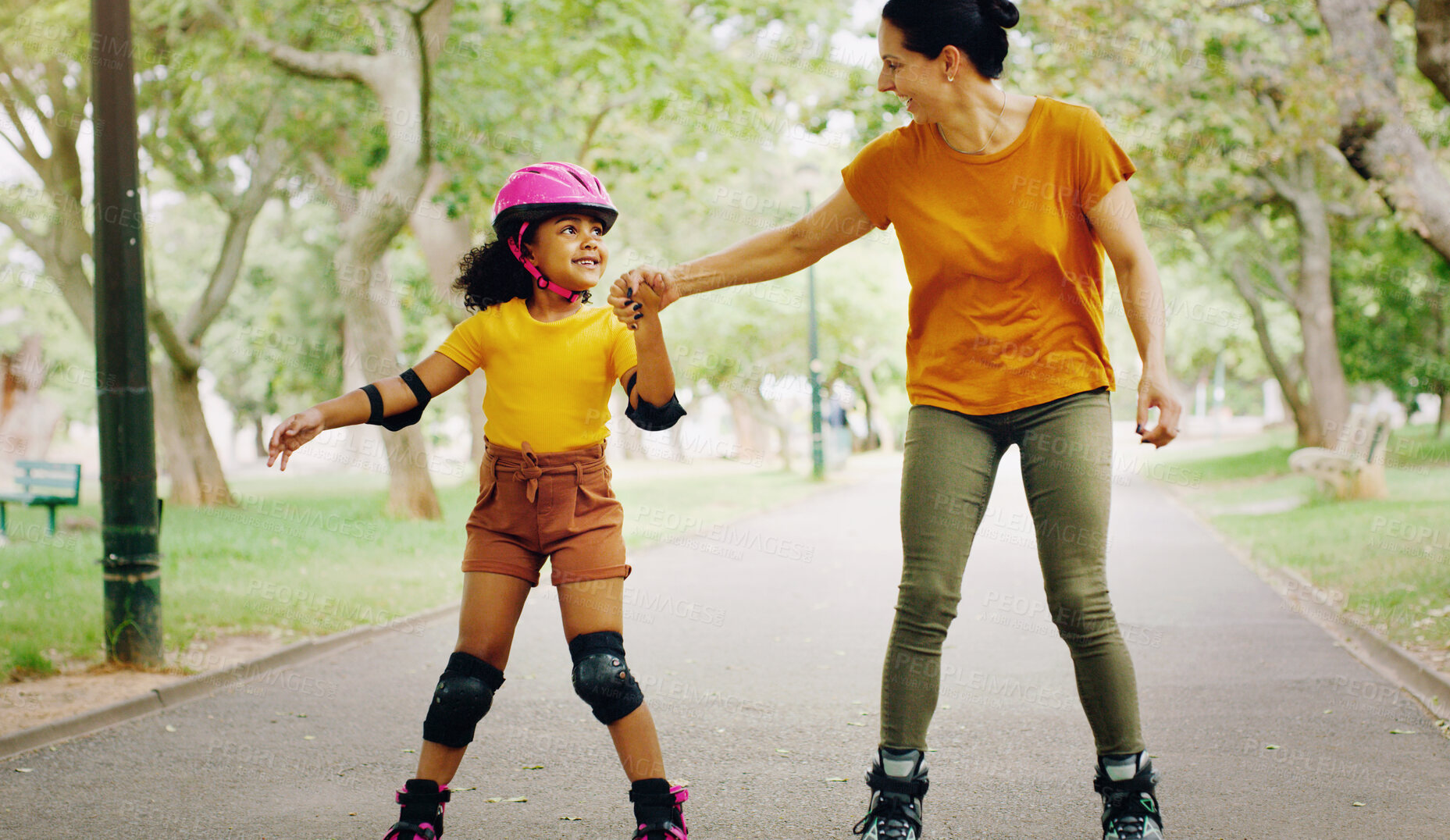 Buy stock photo Mother, park and holding hands to rollerskate with girl child with care, learning and support. Interracial parent, teaching and woman with kid, smile and helping hand on road for skating on holiday
