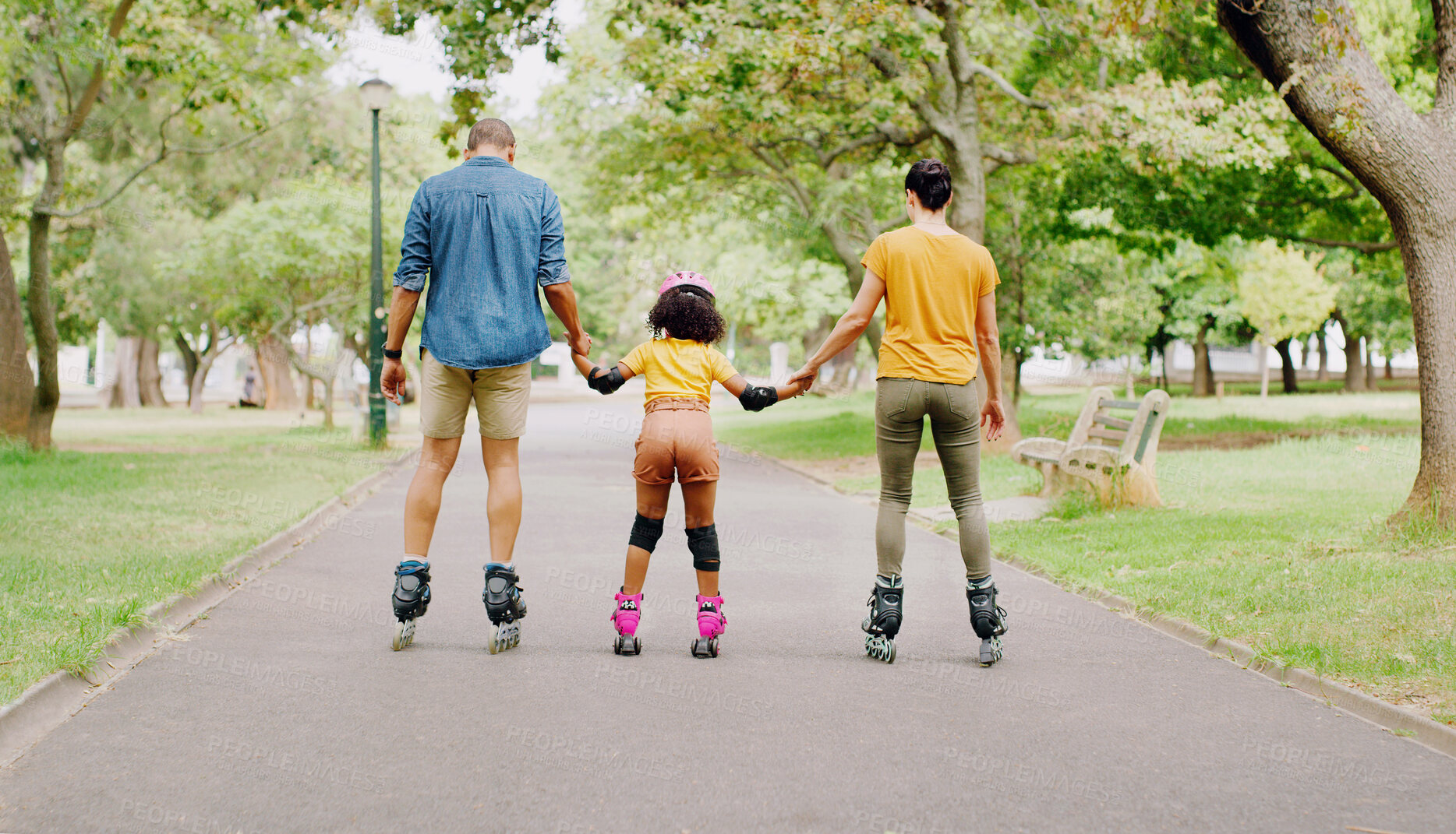Buy stock photo Family, park and holding hands to rollerskate with girl child with care, learning and support. Interracial parents, black man and woman with kid, back and helping hand on road for outdoor holiday