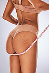 Woman, ass and tape measure in body care, cellulite or weight loss against a gray studio background. Female buttocks measuring size in underwear or lingerie for fitness, diet or healthcare wellness
