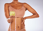 Woman, hands and apple with measuring tape for healthy diet or weight loss against a gray studio background. Female in underwear holding fruit for slim dieting health, body care or wellness nutrition