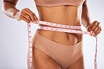 Waist, tape and woman measuring body to lose weight isolated on grey studio background. Fitness, health and hands of a girl on a diet to measure stomach for exercise results and slimming on backdrop