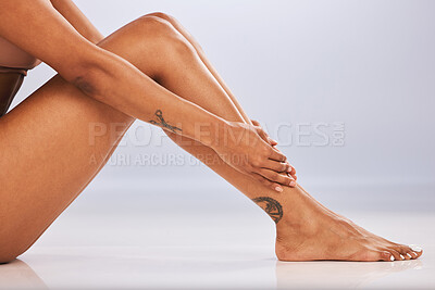 Buy stock photo Hands, legs and tattoo with a black woman in studio, sitting on the floor against a gray background for skincare. Fitness, beauty and body with a female posing for epilation or laser hair removal